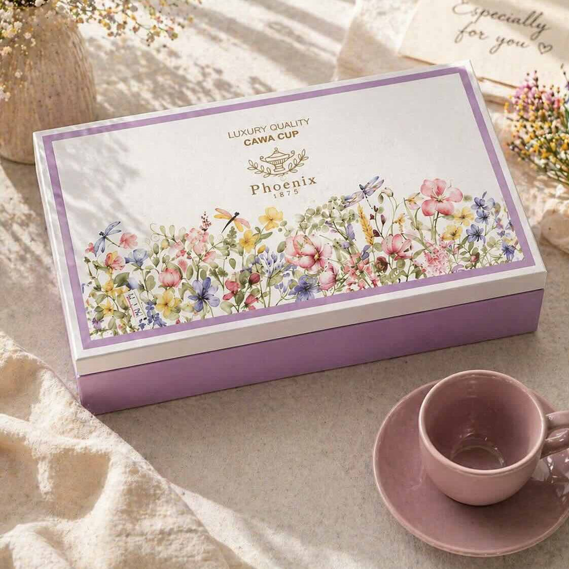 Cana Cup Phoenix tea box with floral design on a table with a pink cup and saucer.