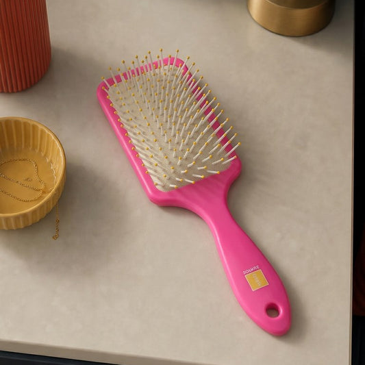 Pink hairbrush on a table with a plant and lamp in the background