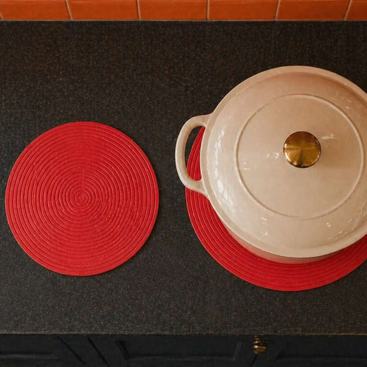 White pot with a lid on a red trivet on a black surface.
