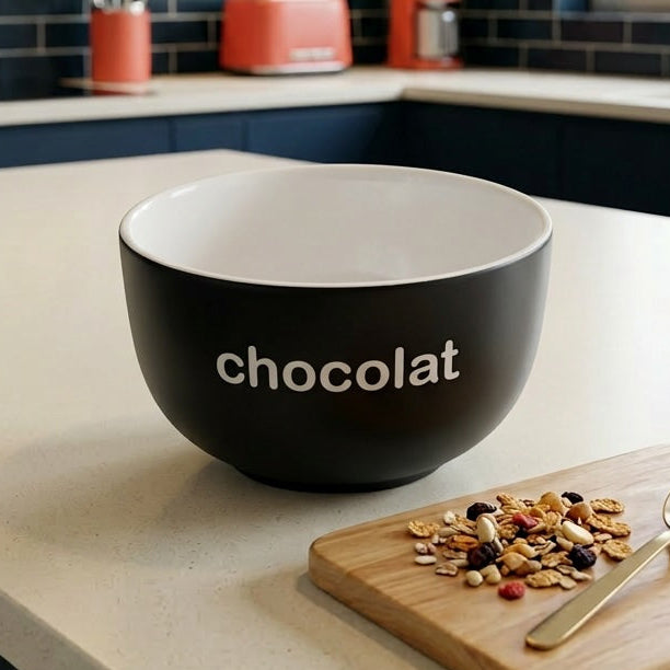 Black 'chocolat' bowl on a kitchen counter with a wooden cutting board and spoon.