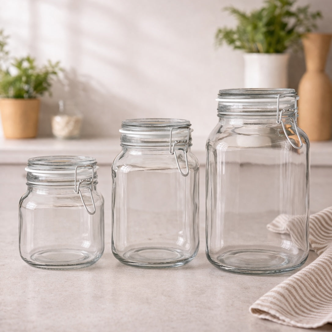Three clear glass jars with metal clips on a light surface with plants in the background