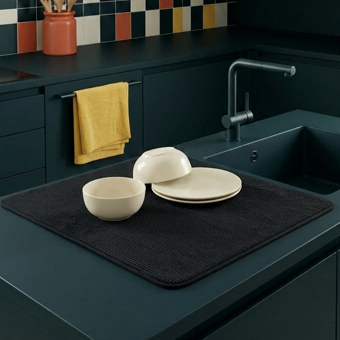Modern kitchen with dark green cabinets, colorful tiled backsplash, and white dishes on a black mat.
