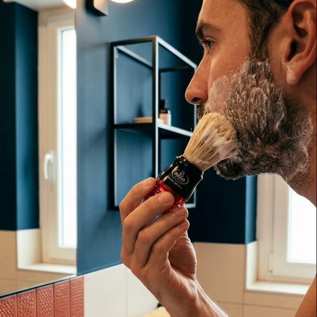 Man shaving with a brush and razor in a bathroom.