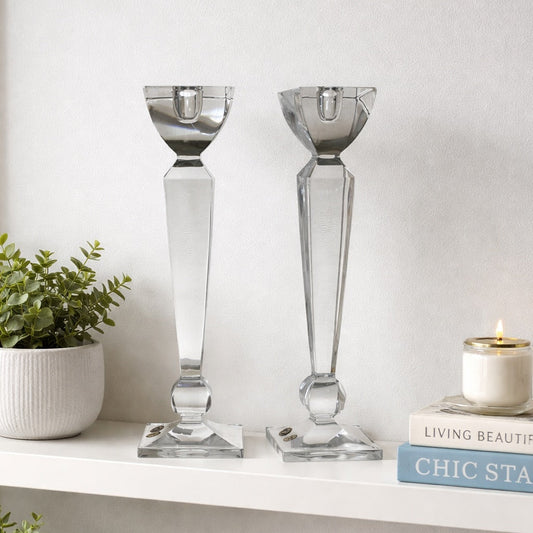 Two crystal candle holders on a white shelf with books and a plant.