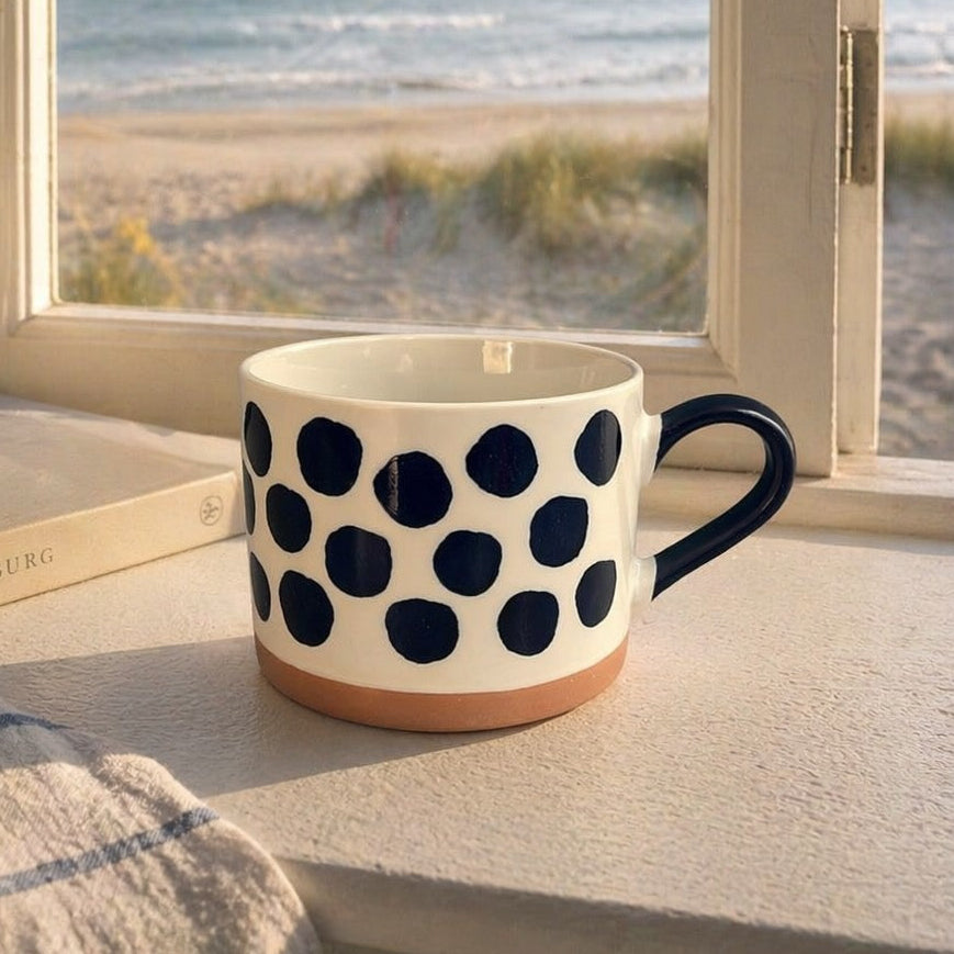 Polka dot mug on a windowsill with a view of the beach