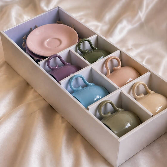 Set of colorful ceramic cups and saucers in a box on a beige fabric background