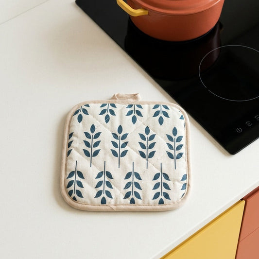 Red pot on a stove with a matching pot holder featuring leaf pattern on a kitchen counter.