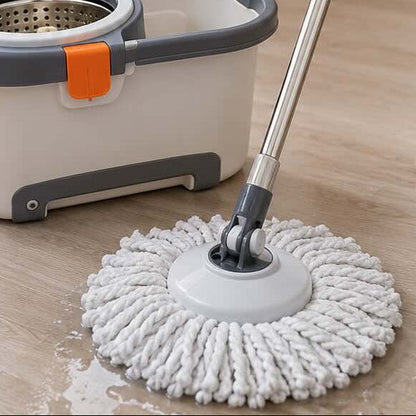 A person in beige pajamas mops a light wood floor with a white and gray twist-mop bucket cleaner in a bright, modern living room.