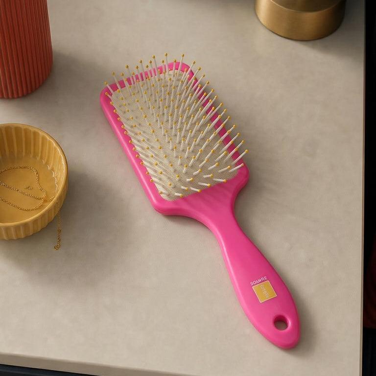 Pink hairbrush on a table with a plant and lamp in the background
