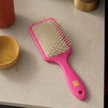 Pink hairbrush on a table with a plant and lamp in the background