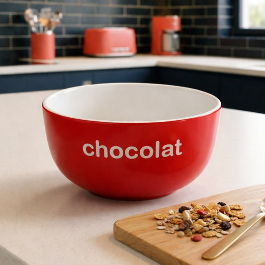 Red bowl labeled 'chocolat' on a kitchen counter with a spoon and snack mix.