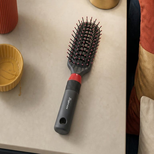 Hairbrush on a table next to a small plant and lamp
