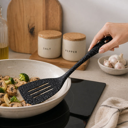 Person using a black spatula to serve food from a pan on a kitchen counter.