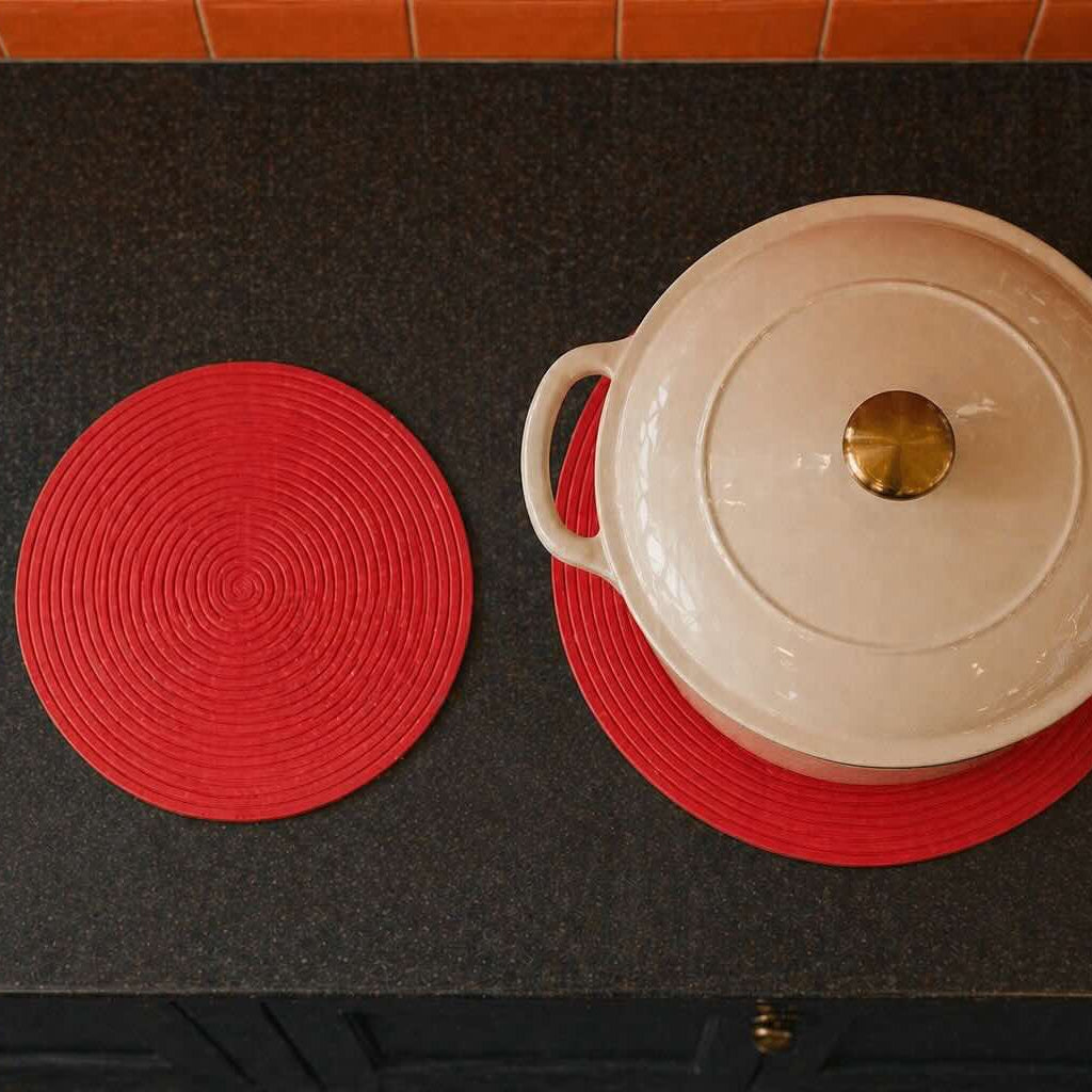 White pot with a lid on a red trivet on a black surface.
