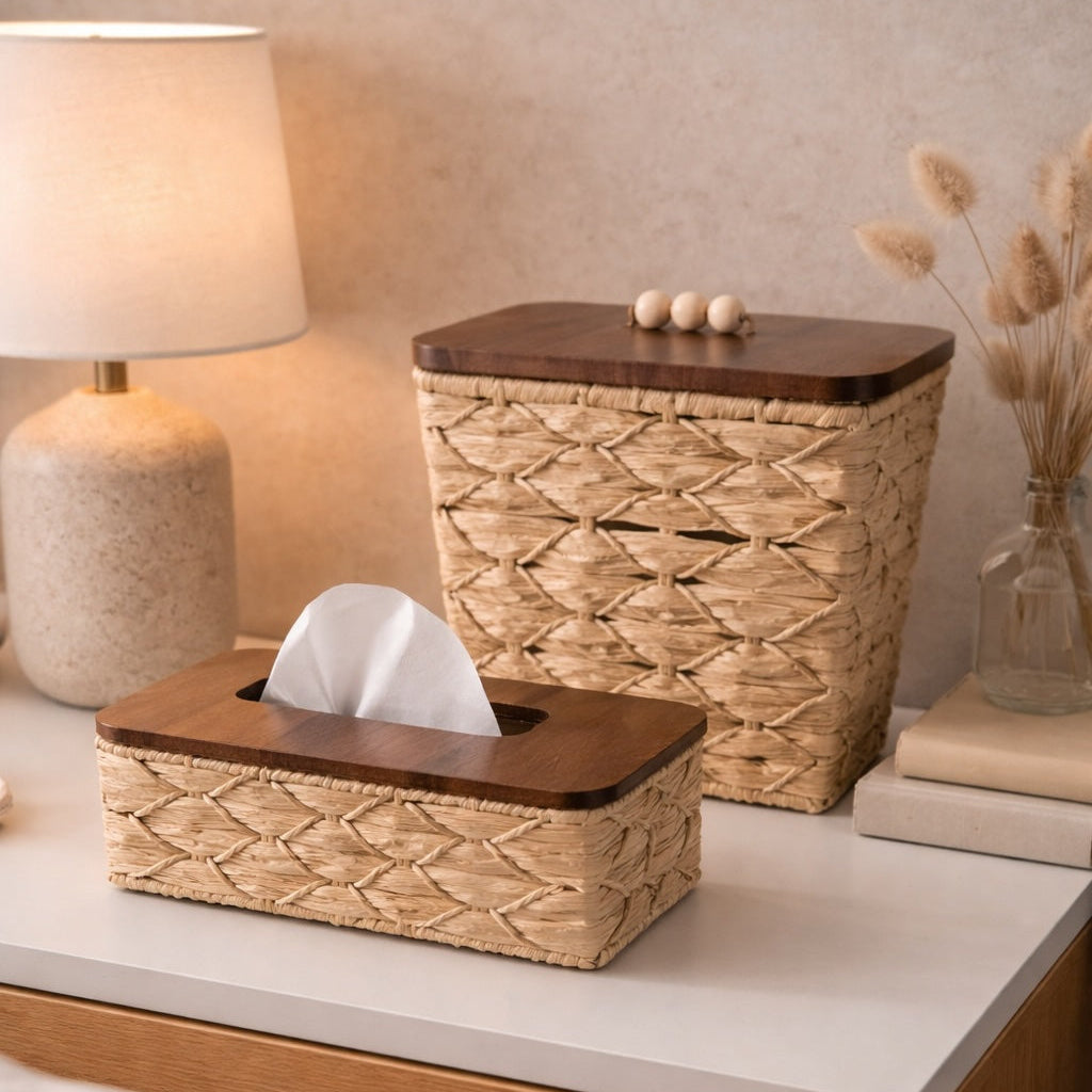 Woven tissue box and trash can on a nightstand with a lamp and decorative items.